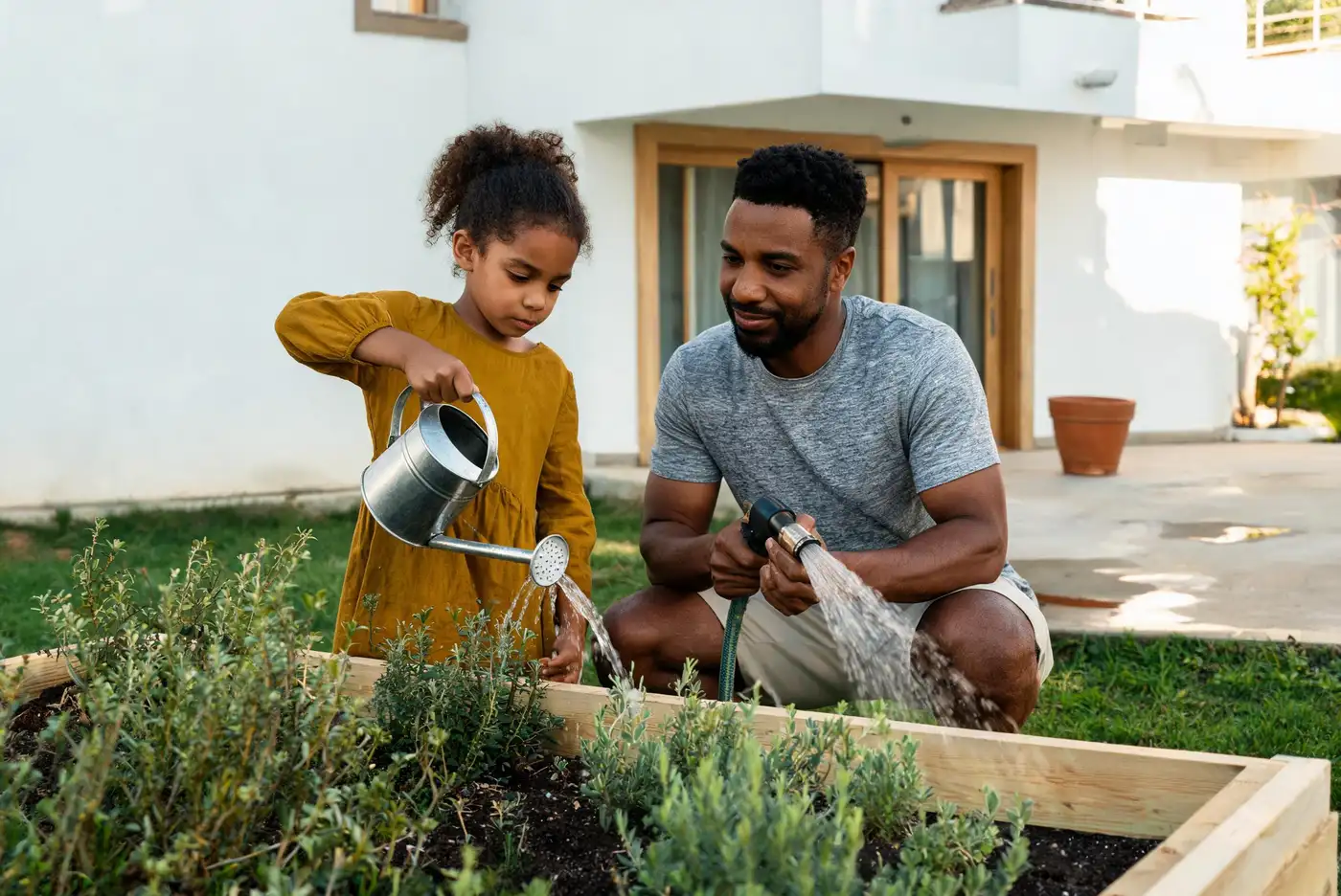 Pai e filha regam as plantas no quintal de uma casa